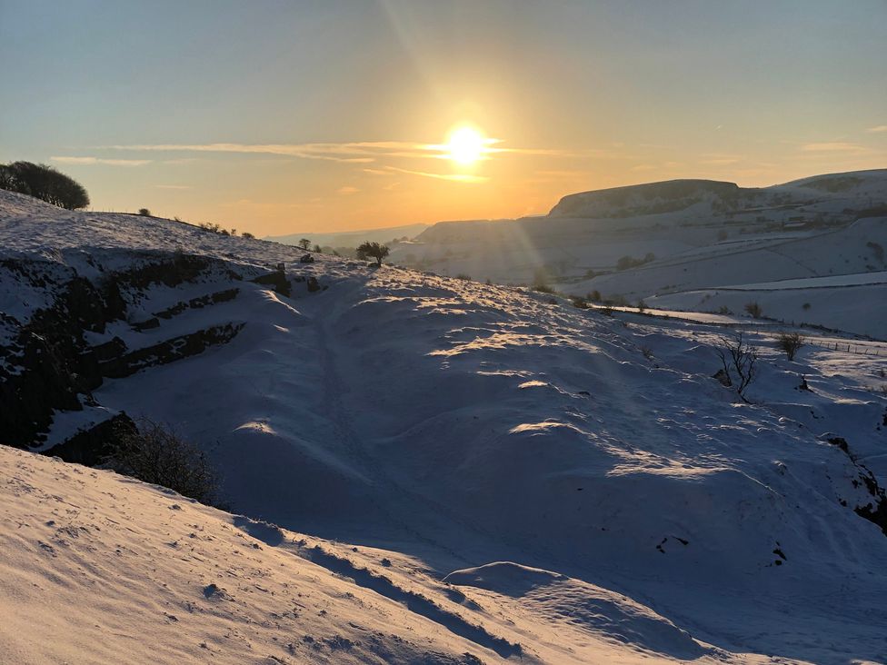A snowy landscape with a setting sun at Woodland View in Buxton