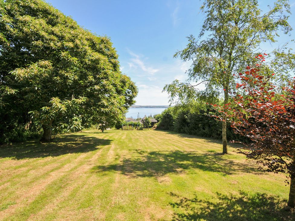 A garden with trees and a view of the water at Jolly Crabber in Porthpean near St Austell