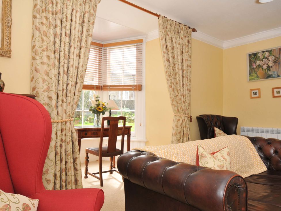 A living room with a wing chair and a desk at Smugglers in Porthpean near St Austell