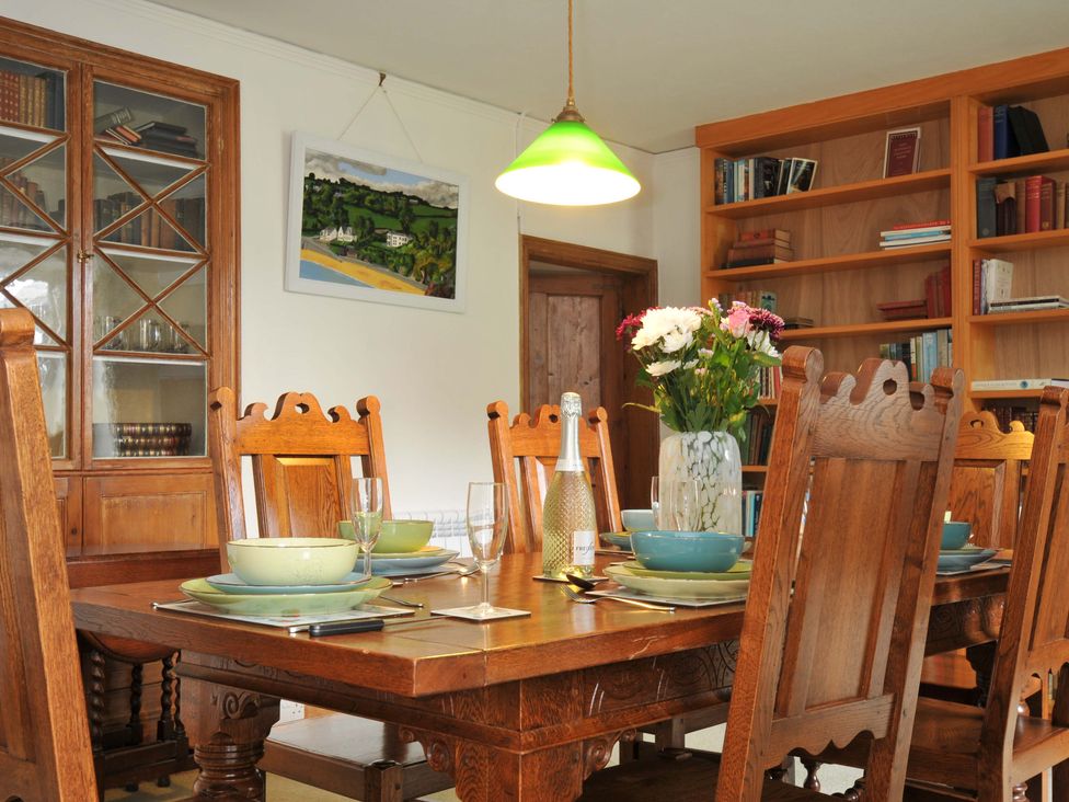 A dining room with a large wooden table and bookshelf at Smugglers in Porthpean near St Austell
