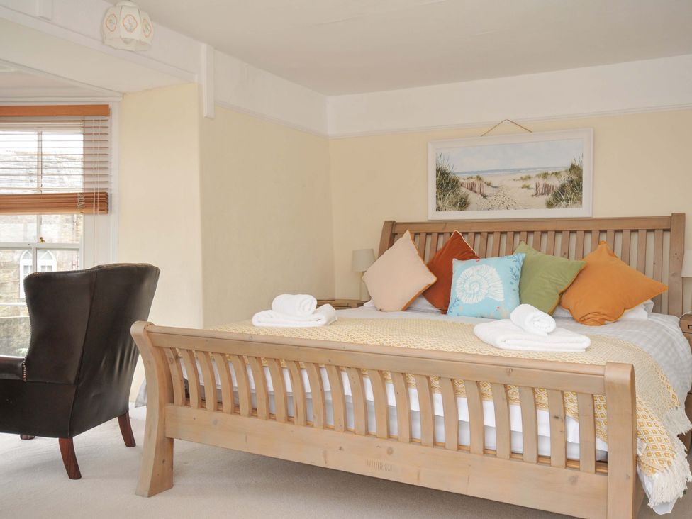 A bedroom with a wooden bed and armchair at Smugglers in Porthpean near St Austell