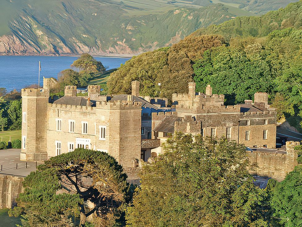 A castle surrounded by trees with a view of water and mountains at Watermouth Castle, Penn-Curzon Apartment Berrynarbor near Ilfracombe