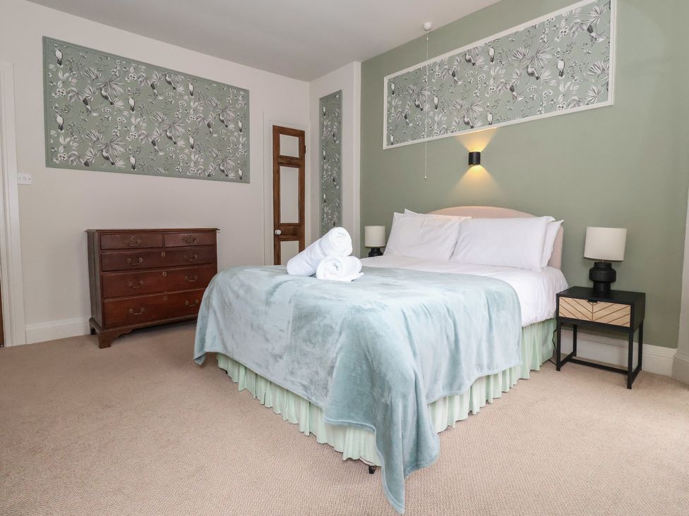 A bedroom with a bed, dresser, and wall art at Watermouth Castle, Penn-Curzon Apartment Berrynarbor near Ilfracombe