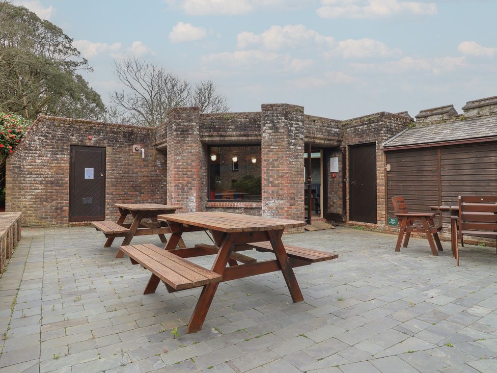 An outdoor seating area with tables and benches at Watermouth Castle, Rhododendron Apartment in Berrynarbor near Ilfracombe
