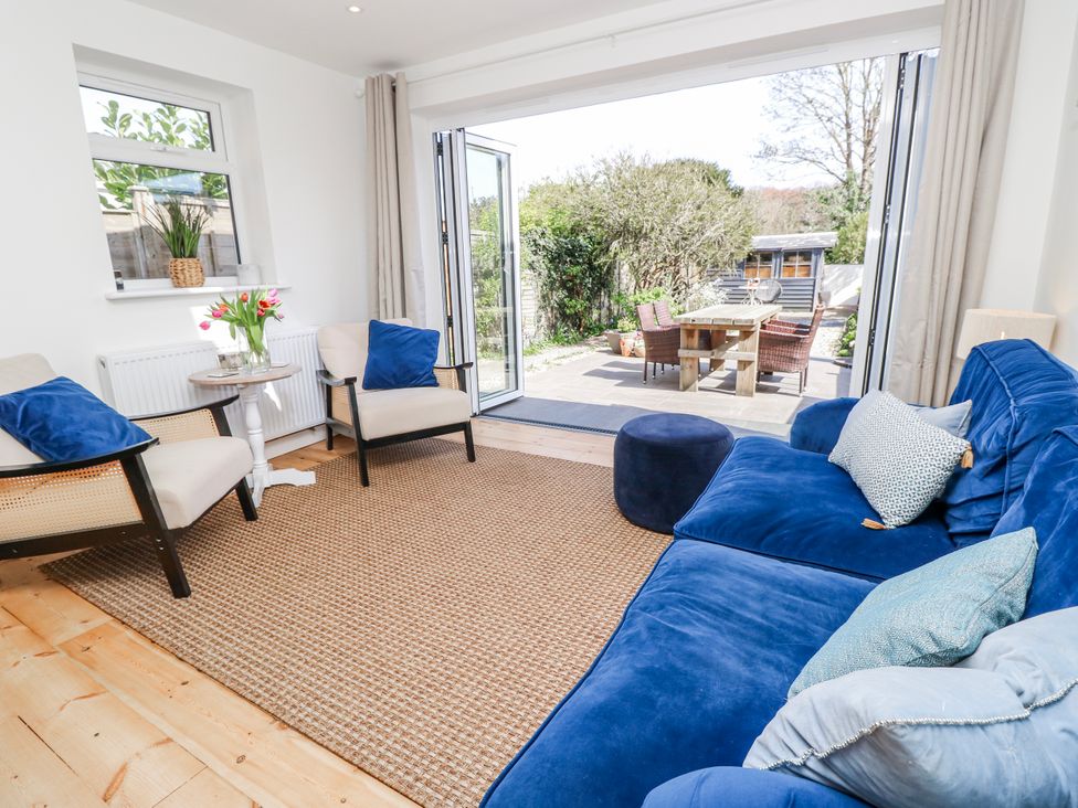 A living room with a blue sofa and chairs facing an outdoor area at 4 Copse Lane Freshwater