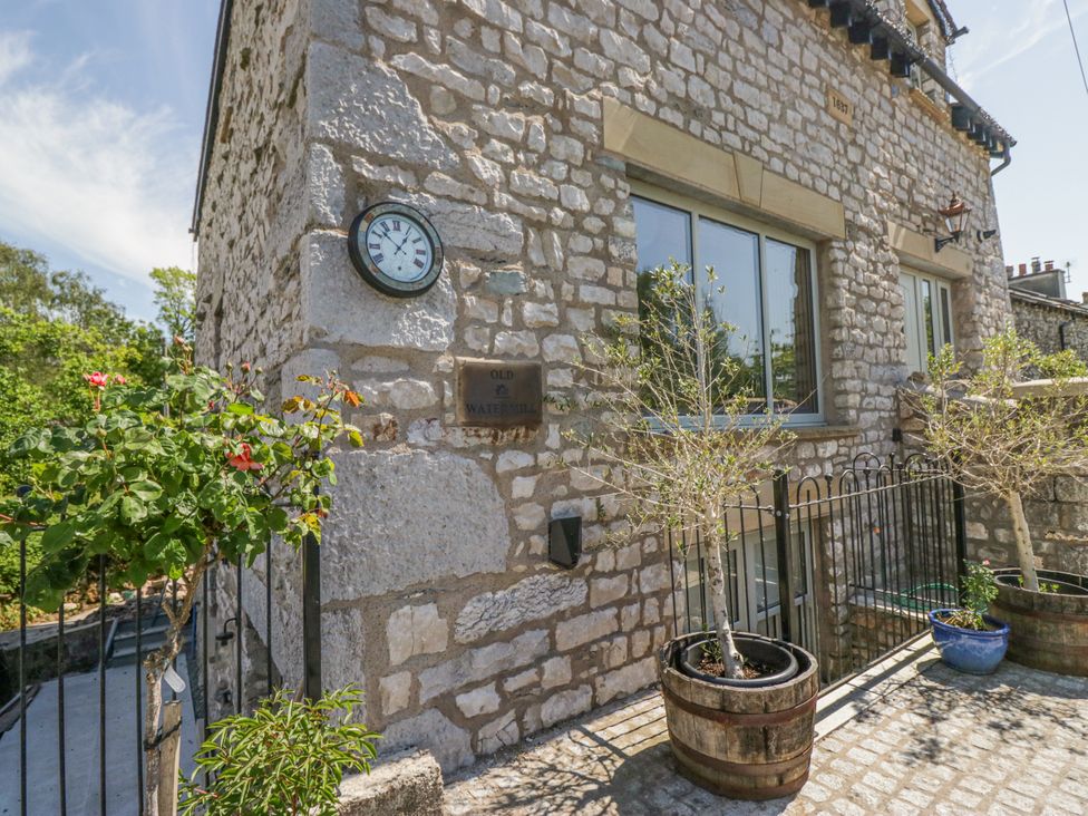 An outdoor view of a stone building with a clock and potted plants at the Old Watermill in Cartmel