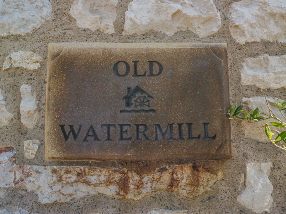 A stone sign labeled Old Watermill on a stone wall at Old Watermill in Cartmel