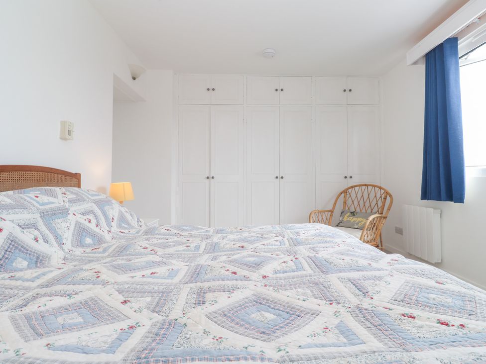 A bedroom with a bed, lamp, wardrobe, chair, and curtain at Flat 2, Moonrakers St. Ives