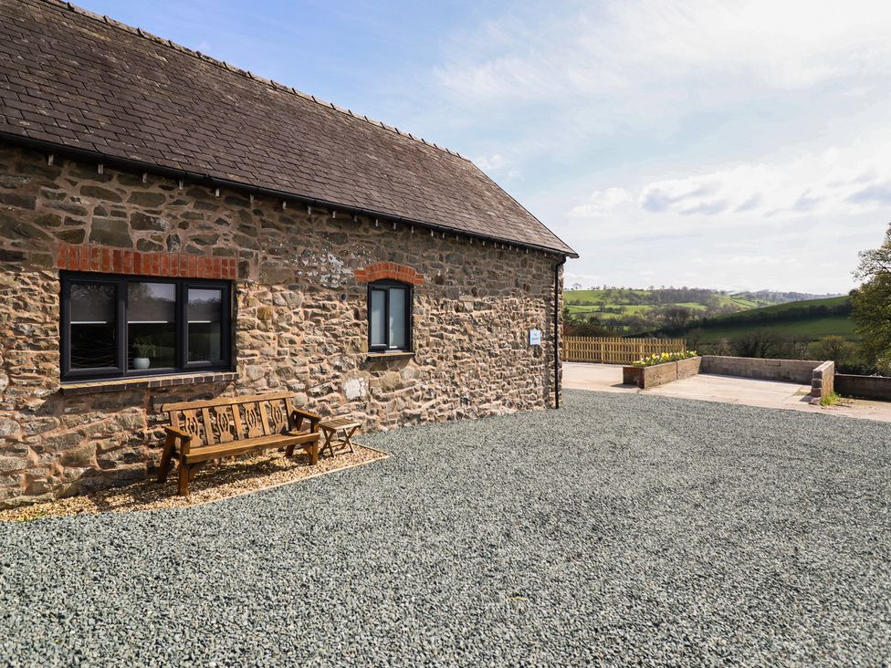 An outdoor view of a stone building with a wooden bench at The Granary Llangyniew near Llanfair Caereinion