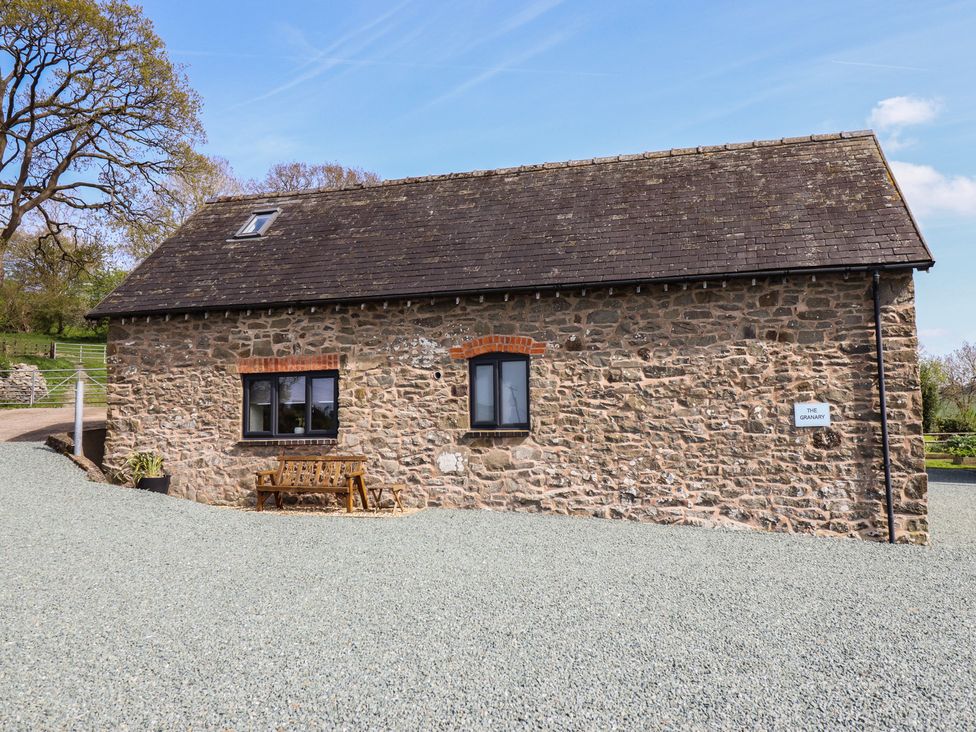 An exterior view of a stone building with a bench at The Granary in Llangyniew near Llanfair Caereinion