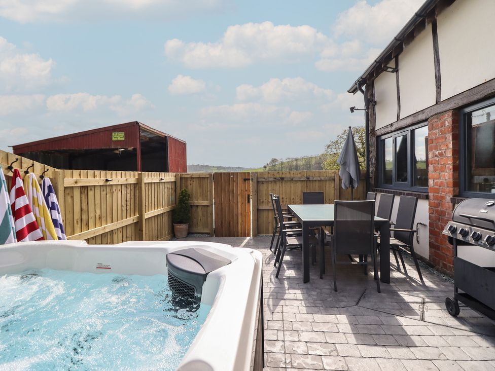 An outdoor area featuring a hot tub, dining table, chairs, and barbecue grill at The Granary Llangyniew near Llanfair Caereinion