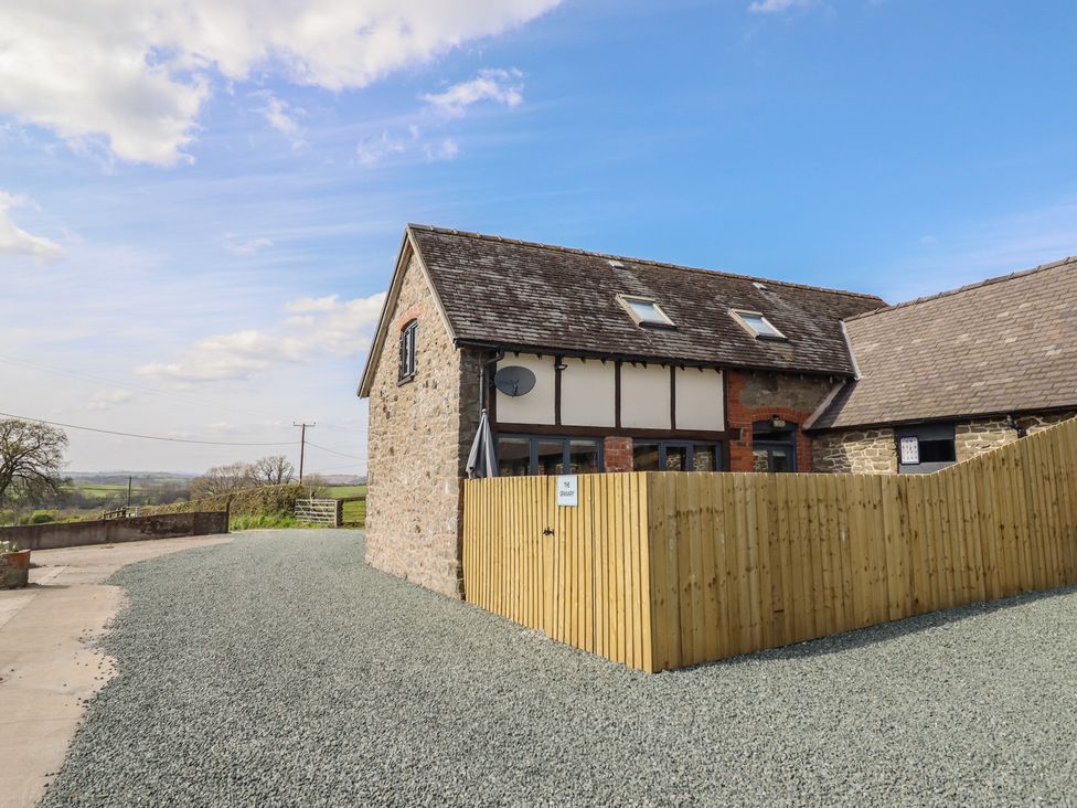 A building with a gravel driveway and wooden fence at The Granary in Llangyniew near Llanfair Caereinion