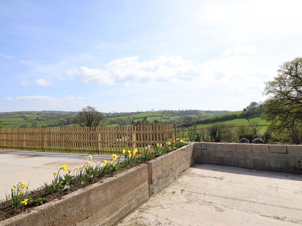 An outdoor area with flowers, a fence, and hills at The Granary in Llangyniew near Llanfair Caereinion