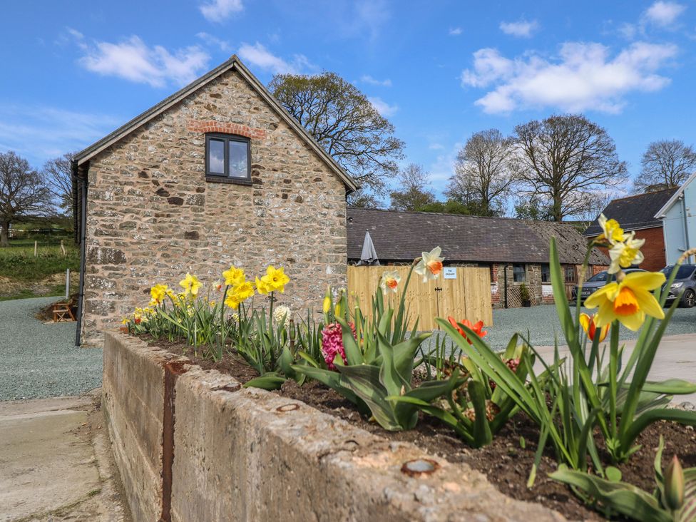 An outdoor view of a stone building with flowers in a garden at The Granary in Llangyniew near Llanfair Caereinion