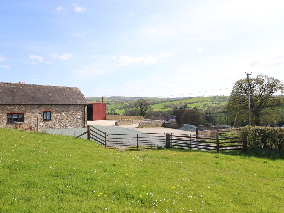A building next to a field with a fence and road at The Granary in Llangyniew near Llanfair Caereinion