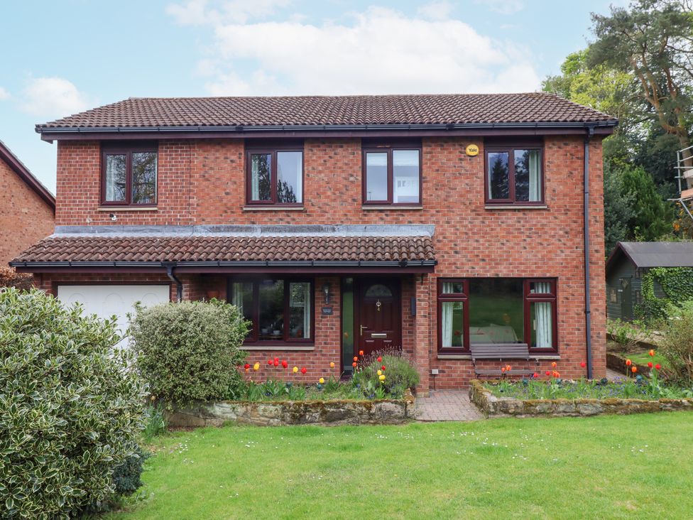 A two story brick house with a tiled roof and a front garden with flowers and bushes at Sparrow House in Alnwick