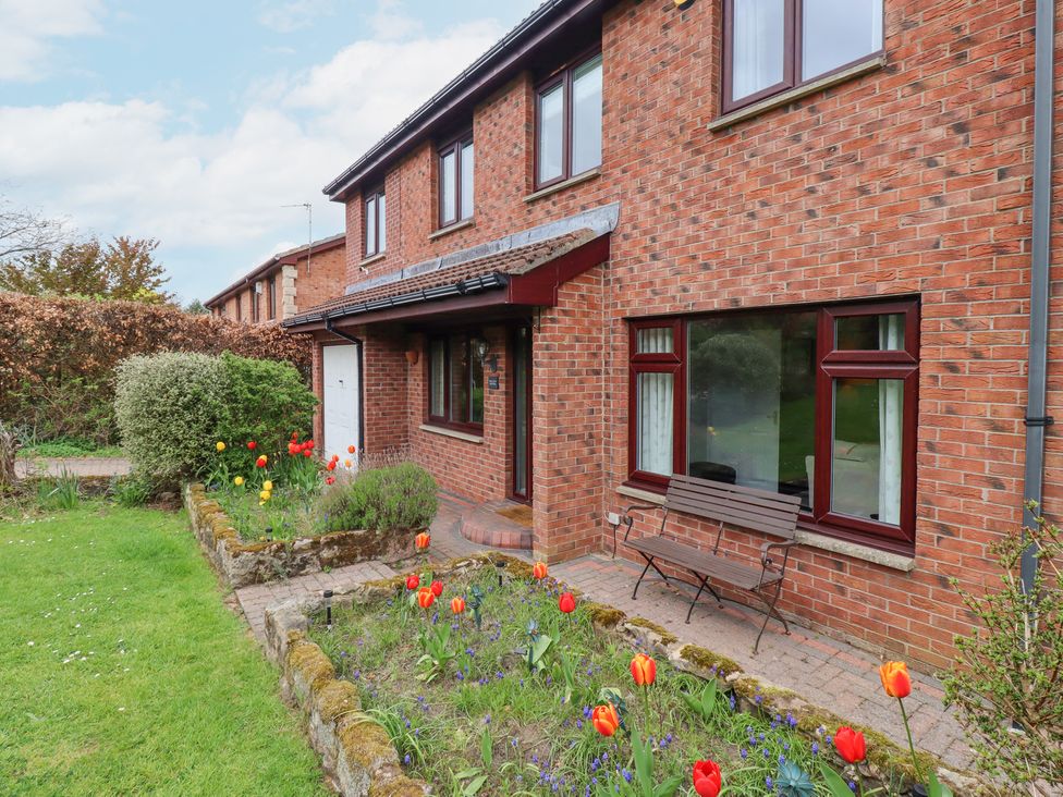 A brick house with a front garden containing flower beds and a bench at Sparrow House in Alnwick