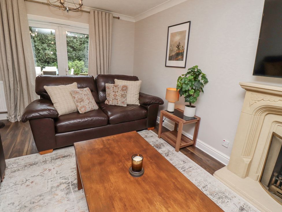 A living room with a brown leather sofa and cushions a wooden coffee table with a candle a small side table with a lamp and plant a fireplace and a wall-mounted TV at Sparrow House in Alnwick