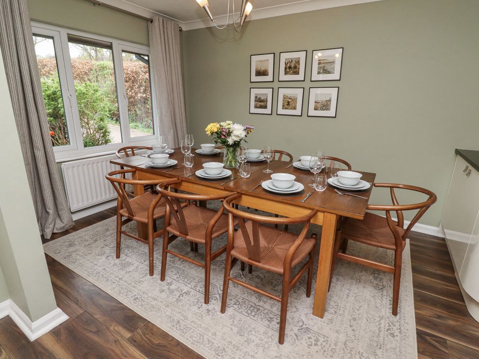 A dining room with a wooden table set with plates bowls glasses and flowers on a rug by a window at Sparrow House in Alnwick