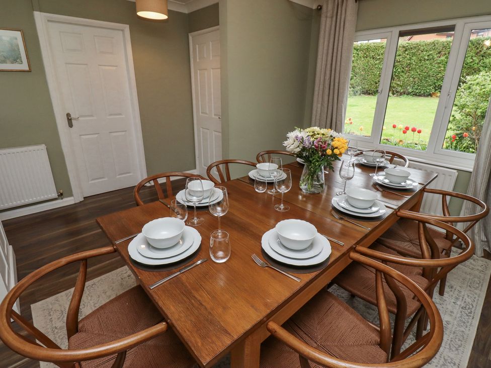 A dining room with a wooden table set with plates bowls glasses and cutlery six wooden chairs and a window with a view of a garden at Sparrow House in Alnwick
