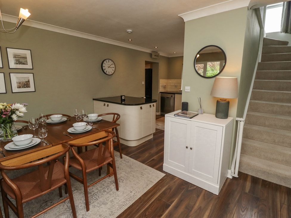 A dining area with a wooden table set for six and a small cabinet with a lamp next to carpeted stairs at Sparrow House in Alnwick
