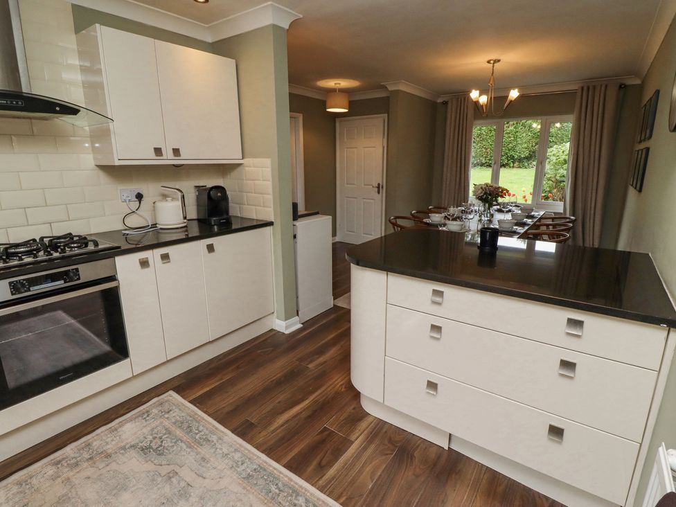 A kitchen and dining area with white cabinets a black countertop a dining table set for meals and a window showing a garden at Sparrow House in Alnwick