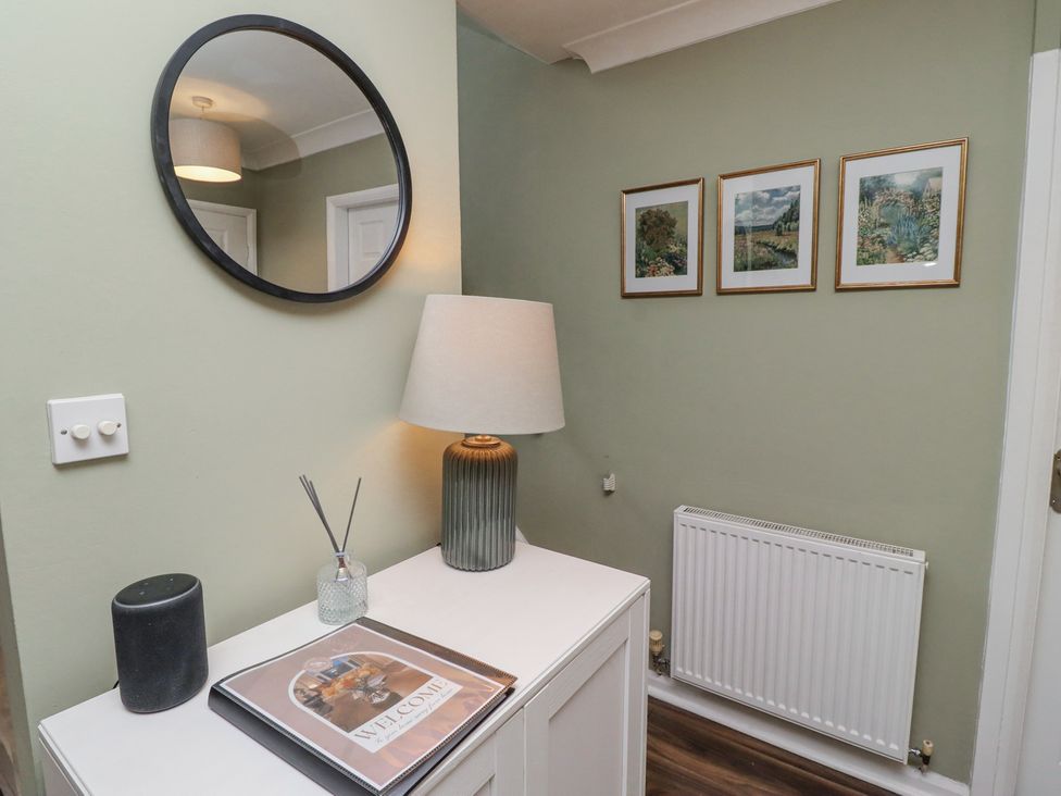A hallway with a round mirror a table lamp a small cabinet and three framed pictures above a radiator at Sparrow House in Alnwick
