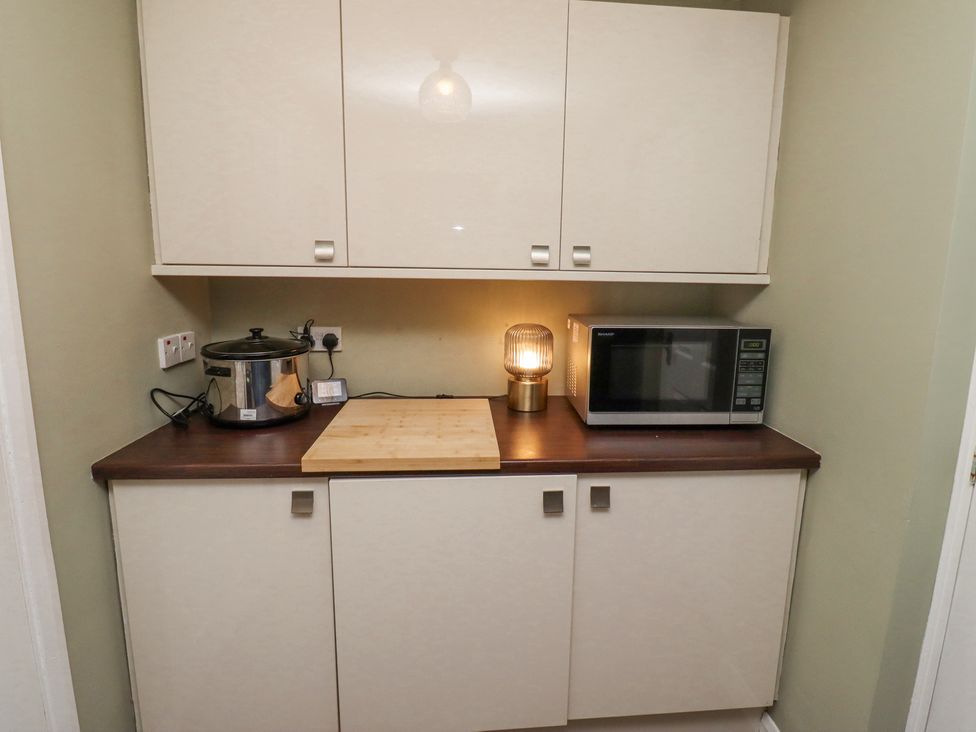 A kitchen countertop with a slow cooker microwave wooden cutting board and a lamp at Sparrow House in Alnwick