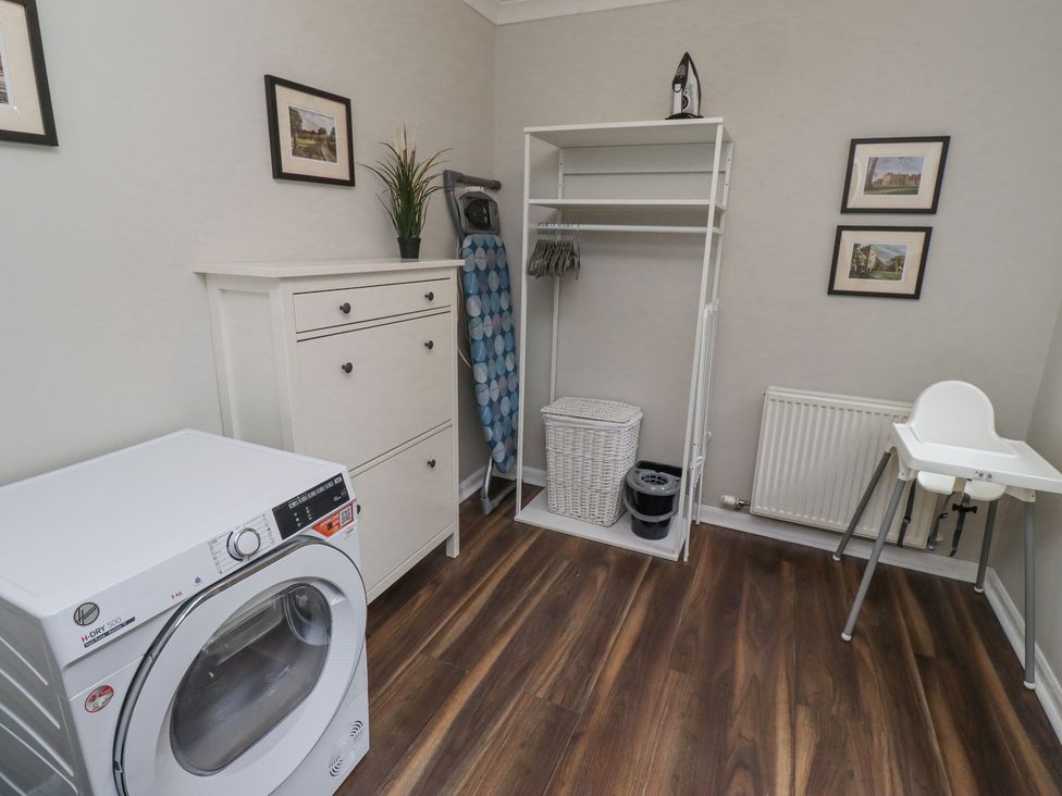 A laundry room with a dryer chest of drawers ironing board and highchair at Sparrow House in Alnwick