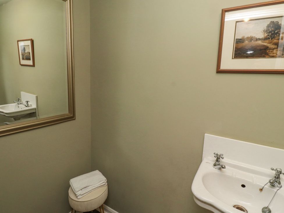 A bathroom with a white sink a round stool with folded towels a large mirror and framed pictures on the wall at Sparrow House in Alnwick
