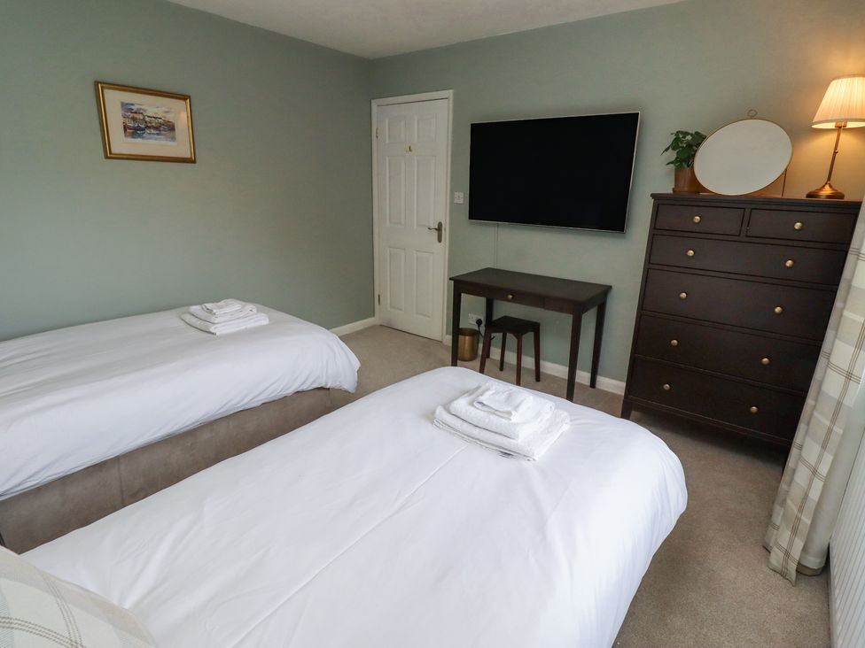 A bedroom with two beds white bedding a chest of drawers a wall mounted tv and a small desk at Sparrow House in Alnwick