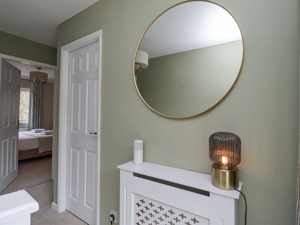A hallway with a round mirror above a white radiator cover and a bedroom visible through an open door at Sparrow House in Alnwick