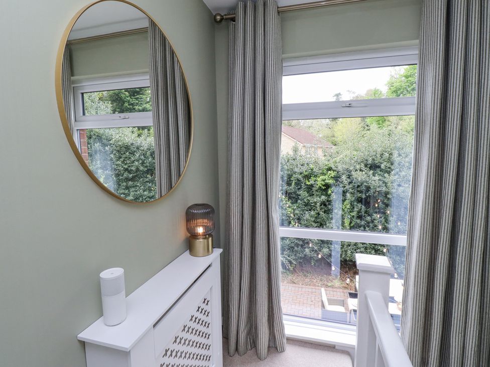 A corner with a round mirror above a white radiator cover and a window with striped curtains at Sparrow House in Alnwick