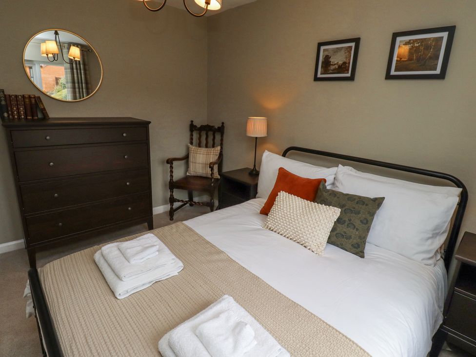 A bedroom with a bed with pillows and folded towels a dark wooden dresser a round mirror and a wooden chair at Sparrow House in Alnwick