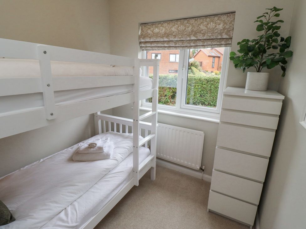 A bedroom with a white bunk bed a chest of drawers with a plant on top and a window showing houses outside at Sparrow House in Alnwick