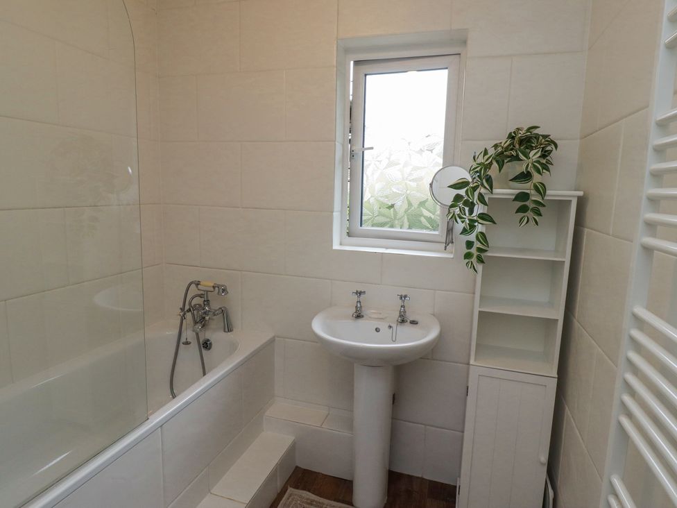 A bathroom with a bathtub a pedestal sink a shelving unit with a plant and a frosted window at Sparrow House in Alnwick