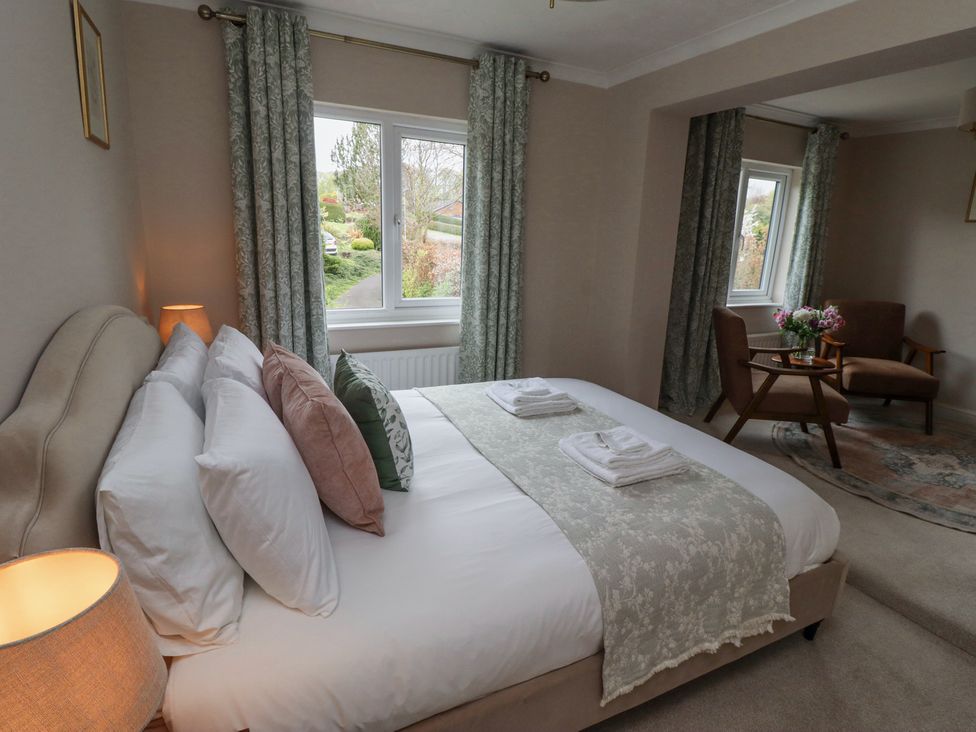 A bedroom with a bed and pillows beside a window and two chairs with a small table with flowers at Sparrow House in Alnwick
