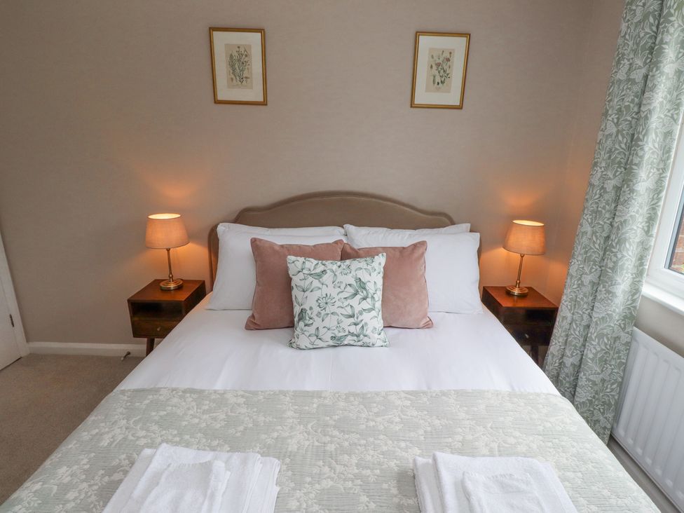 A bedroom with a double bed two side tables with lamps two framed pictures on the wall and patterned curtains at Sparrow House in Alnwick