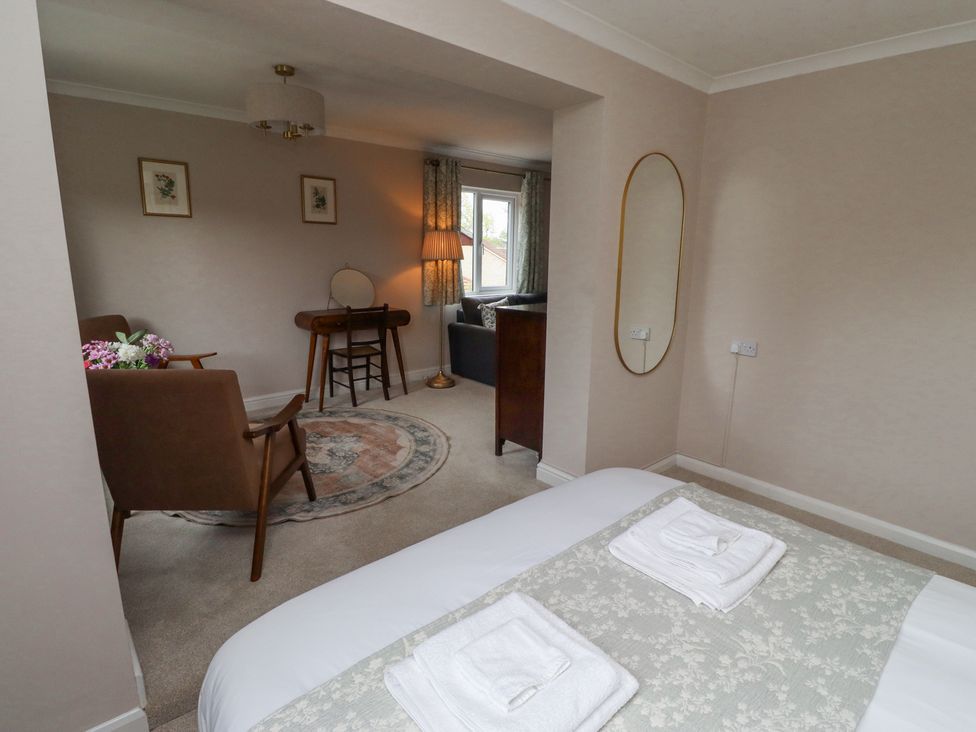 A bedroom with a bed and towels connected to a sitting area with chairs a rug lamp and a dressing table at Sparrow House in Alnwick
