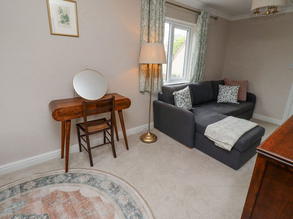 A room with a dark gray sofa and floral cushions a wooden dressing table with a round mirror and chair a floor lamp and a patterned curtain at Sparrow House in Alnwick