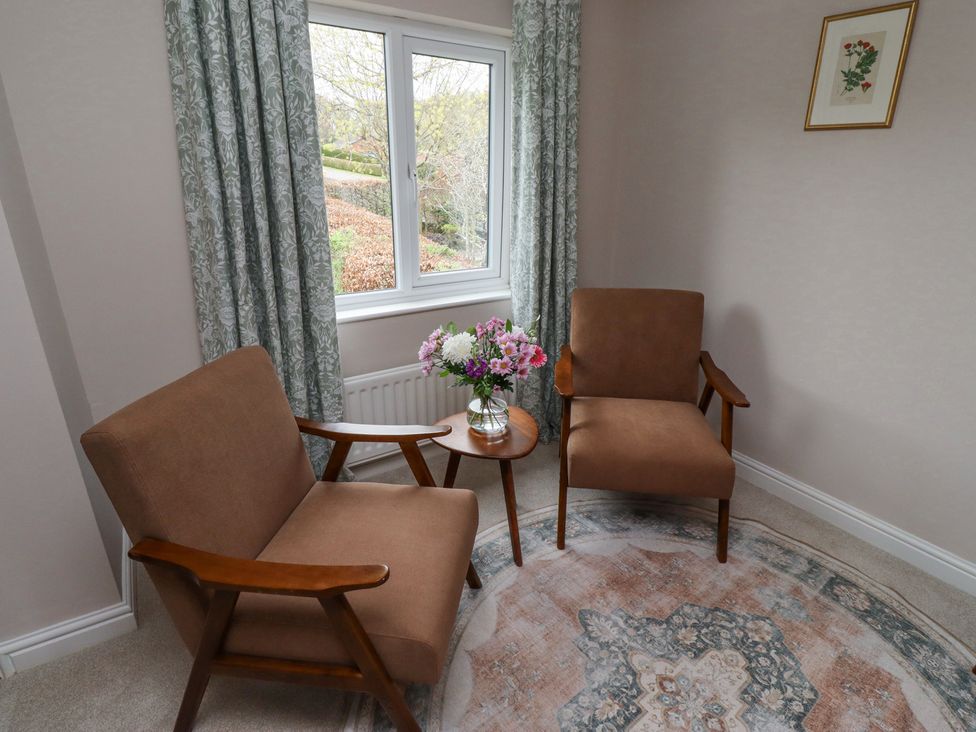 A small sitting area with two armchairs a circular rug and a small table with flowers by a window at Sparrow House in Alnwick