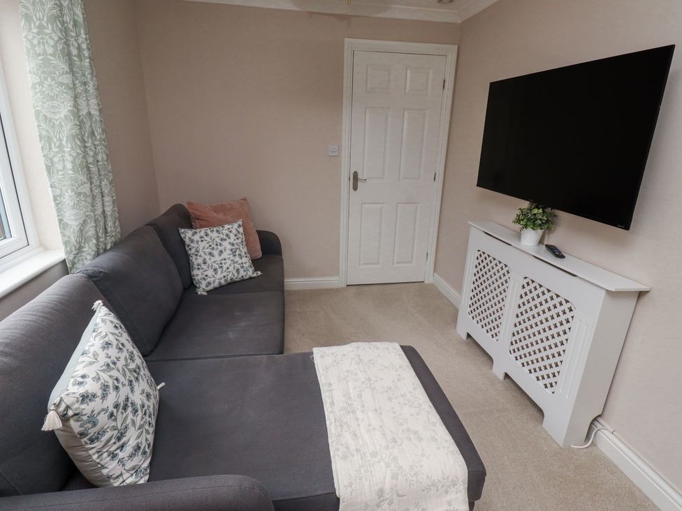 A living room with a dark gray sofa and patterned cushions a white radiator cover with a potted plant and a wall mounted television at Sparrow House in Alnwick