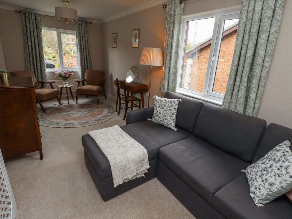 A living room with a gray sofa, two armchairs, a wooden table with flowers, a floor lamp, and patterned curtains at Sparrow House in Alnwick