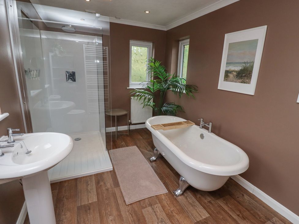 A bathroom with a clawfoot bathtub a shower with glass door a pedestal sink a plant and two windows at Sparrow House in Alnwick