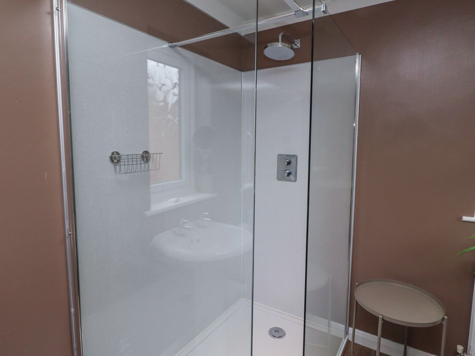A bathroom with a glass shower enclosure a round side table and brown walls at Sparrow House in Alnwick
