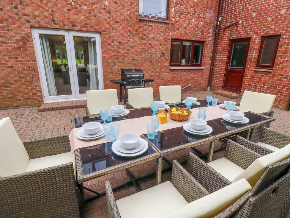 An outdoor dining area with a glass table set with plates bowls and blue glasses surrounded by wicker chairs with cushions at Sparrow House in Alnwick