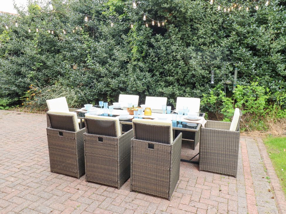 An outdoor dining table with chairs set on a paved patio area with string lights above and bushes behind at Sparrow House in Alnwick