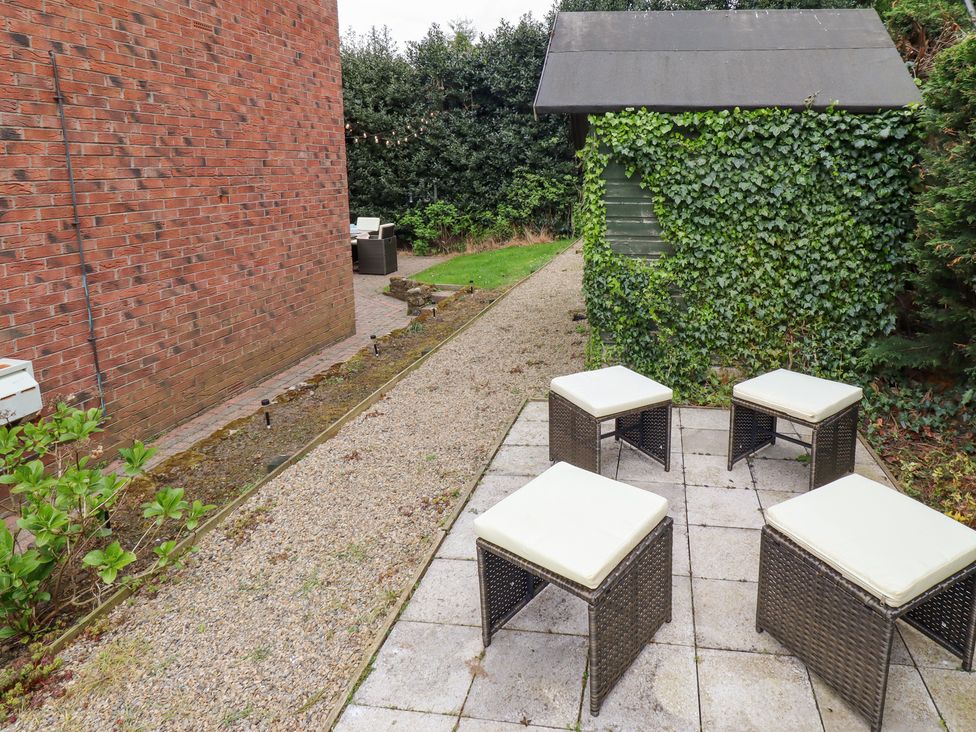 A garden area with four cushioned stools on a tiled patio near a green shed covered in ivy at Sparrow House in Alnwick
