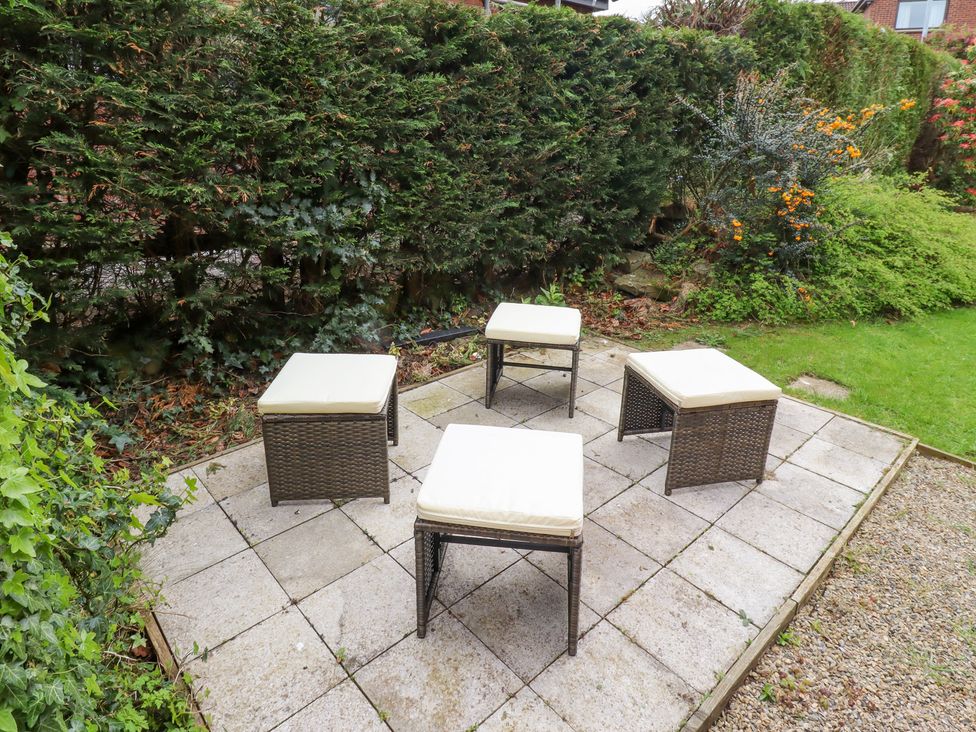 An outdoor seating area with four cushioned stools on a tiled patio surrounded by greenery at Sparrow House in Alnwick