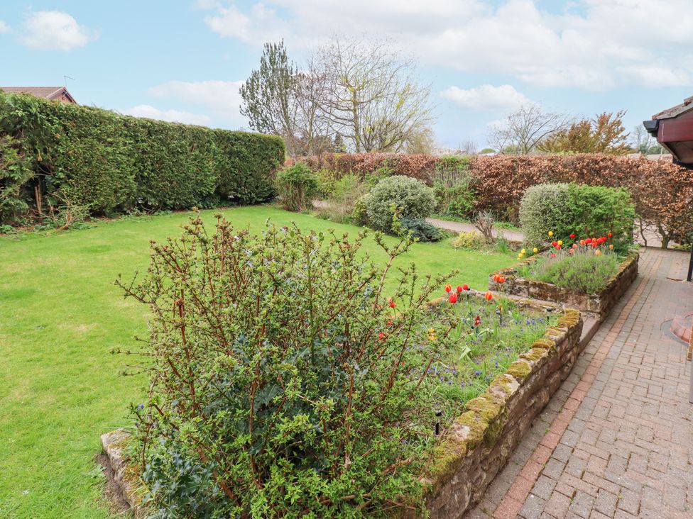 A garden with flower beds and bushes next to a paved pathway at Sparrow House in Alnwick